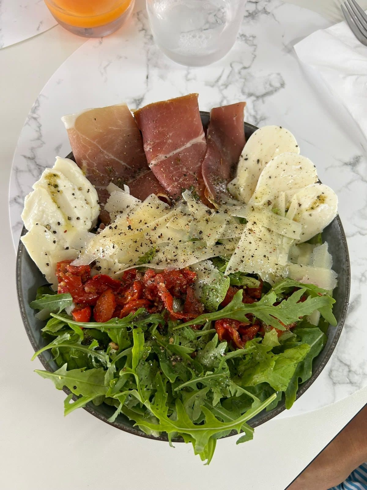 Une assiette de charcuterie italienne avec de la burrata et une salade de roquette.