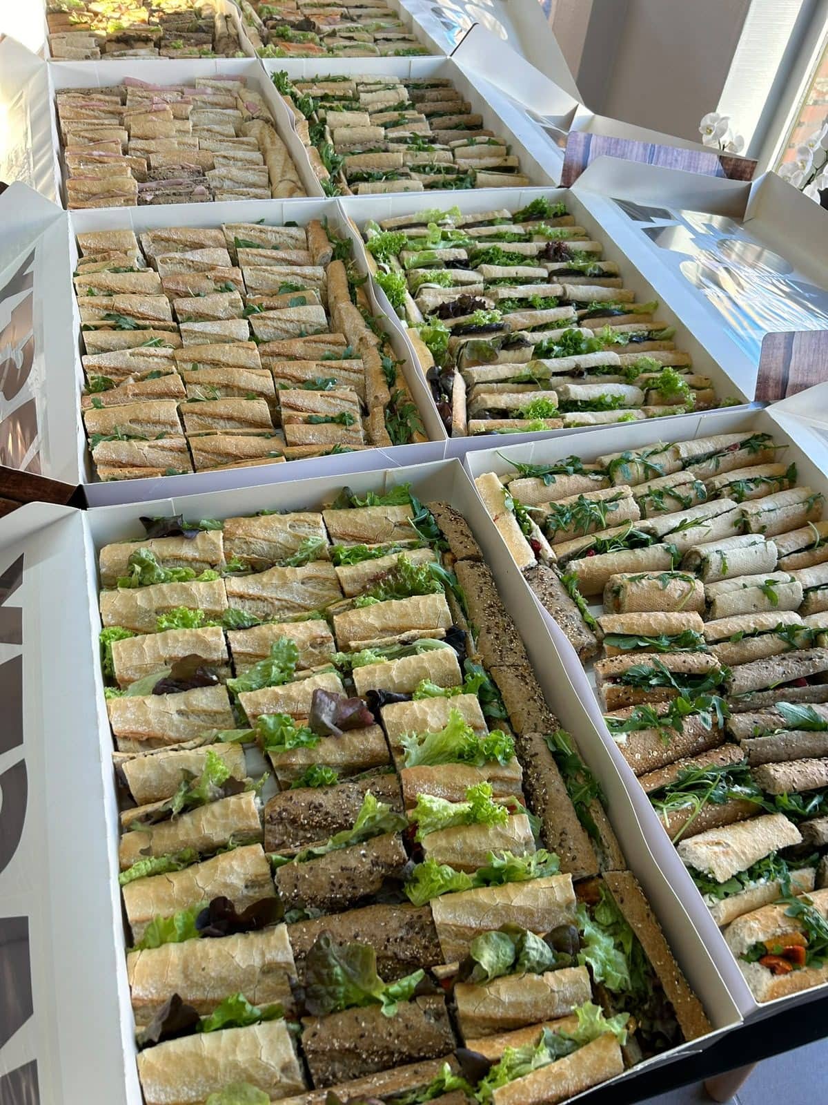 De longs plateaux de mini-sandwichs garnis, alignés côte à côte sur le comptoir.