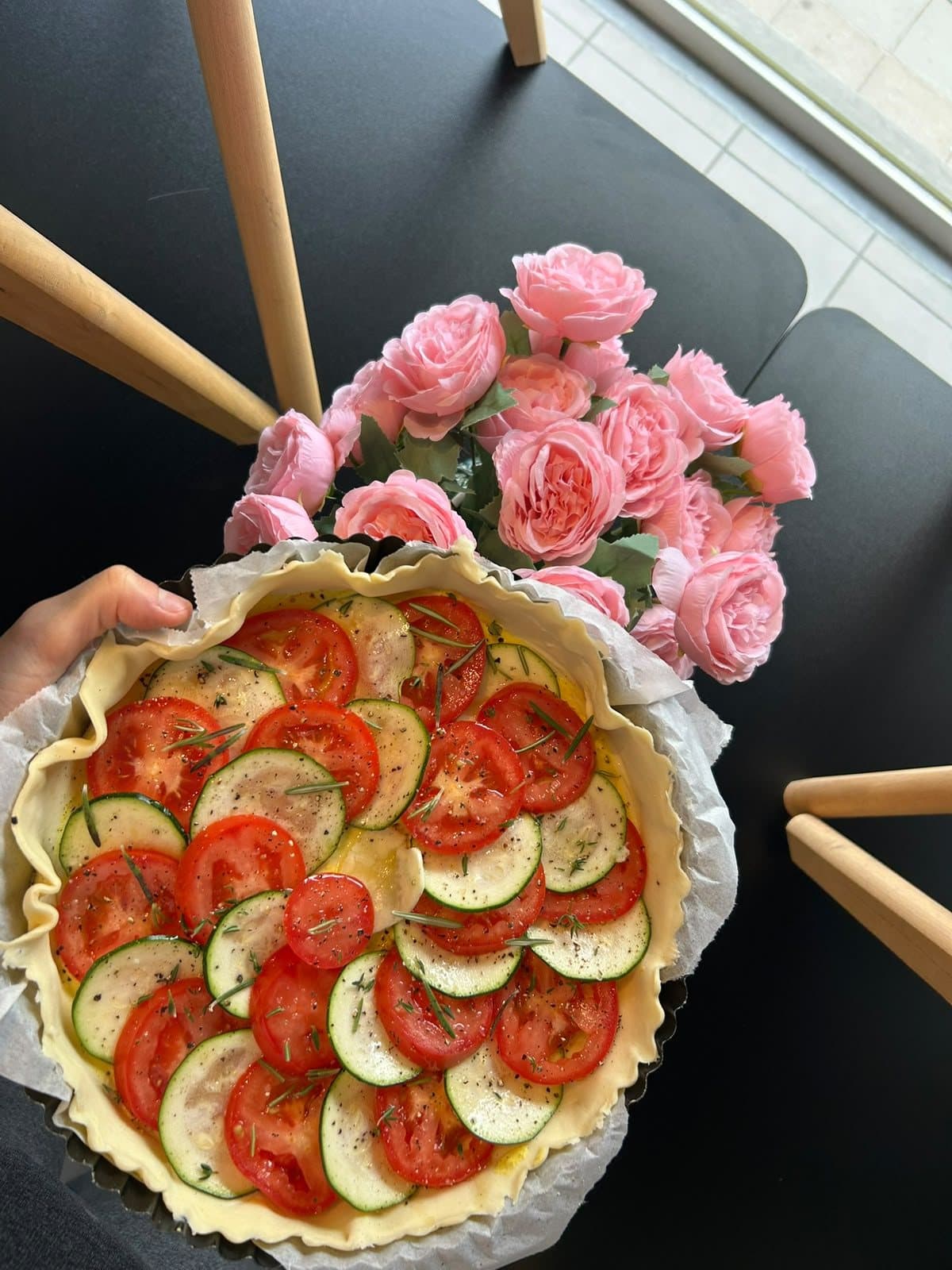 Une tarte aux tomates et aux courgettes, posée près d'un bouquet de roses.